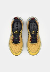 Gule og marineblå sportsko med meshin toppen, struktureret design og røde accenter. Har New Balance-logo og "Hiero" branding på tungen.