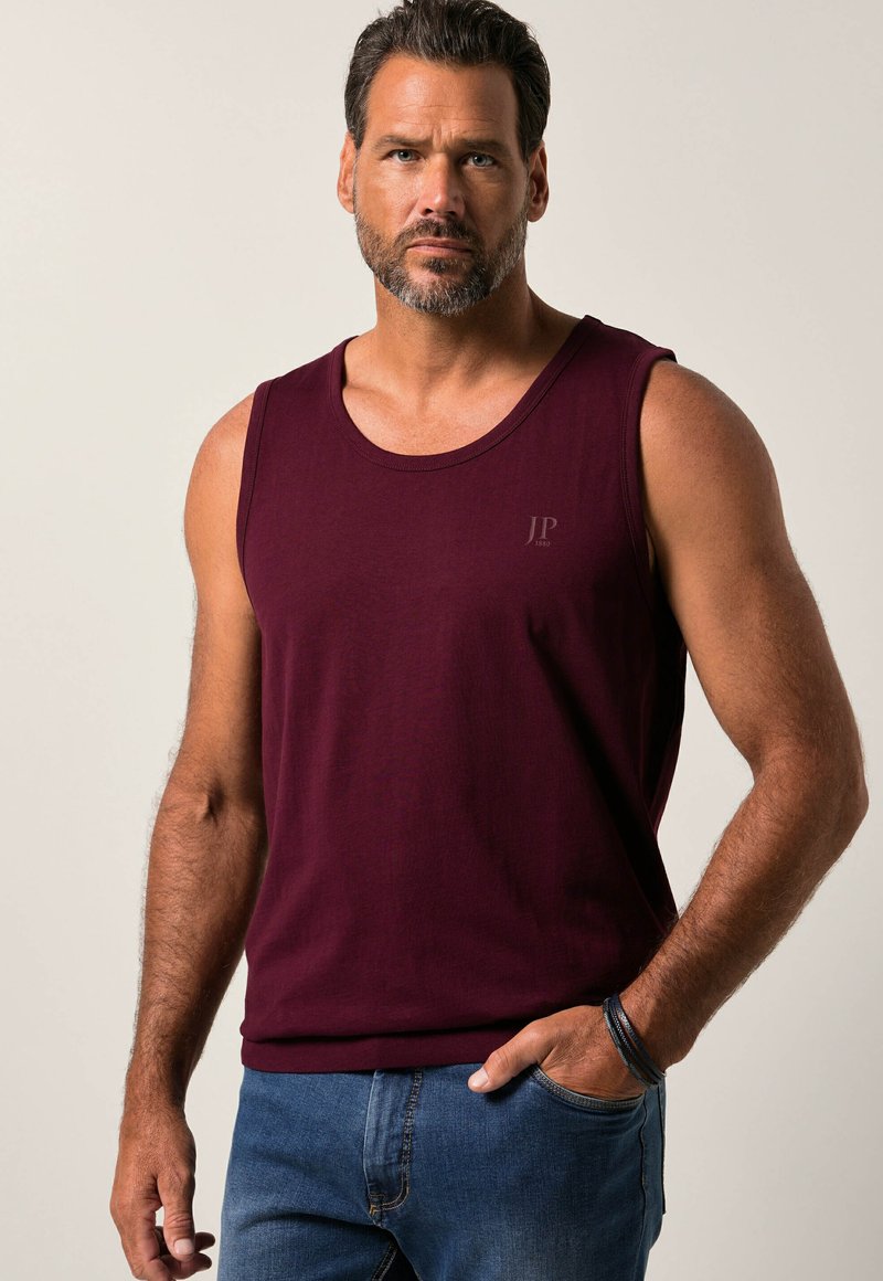 Bordowy bezrękawnik z bawełny, z okrągłym dekoltem i subtelnym szarym logo na piersi; zestawiony z niebieskimi dżinsami.