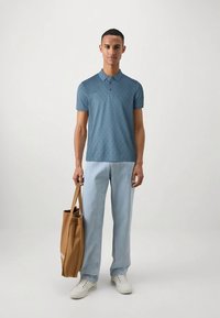 Light blue polo shirt with a textured diamond pattern, paired with light blue jeans and a tan tote bag, featuring a smooth, sturdy fabric.