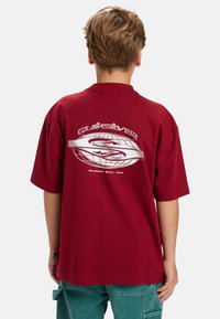 Rode oversized T-shirt met een witte bedrukte logo en wereldbolontwerp op de achterkant, gemaakt van katoen, met korte mouwen en een relaxte pasvorm.