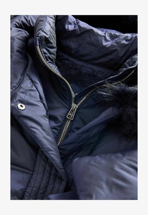 Jachetă puffer bleumarin cu fermoar argintiu, tiv din blană și textură matlasată. Interiorul are un căptușel moale și detalii de cusătură discrete.