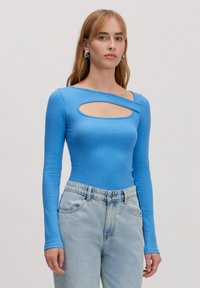 Blauwe lange mouwen bodysuit met een geribbelde textuur en een vooraan uitgesneden ontwerp. Gecombineerd met lichtblauwe high-waisted jeans.