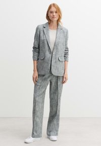 Grijze gepatterneerde pak gemaakt van geweven stof, met een op maat gemaakte blazer met revers, twee voorkruiden en een losse pasvorm broek.