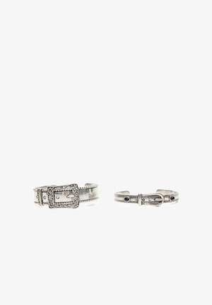 Zwei silberne Manschettenarmbänder in Form von Gürtelriemen mit detaillierten Schnallen und dekorativen Mustern auf weißem Hintergrund.