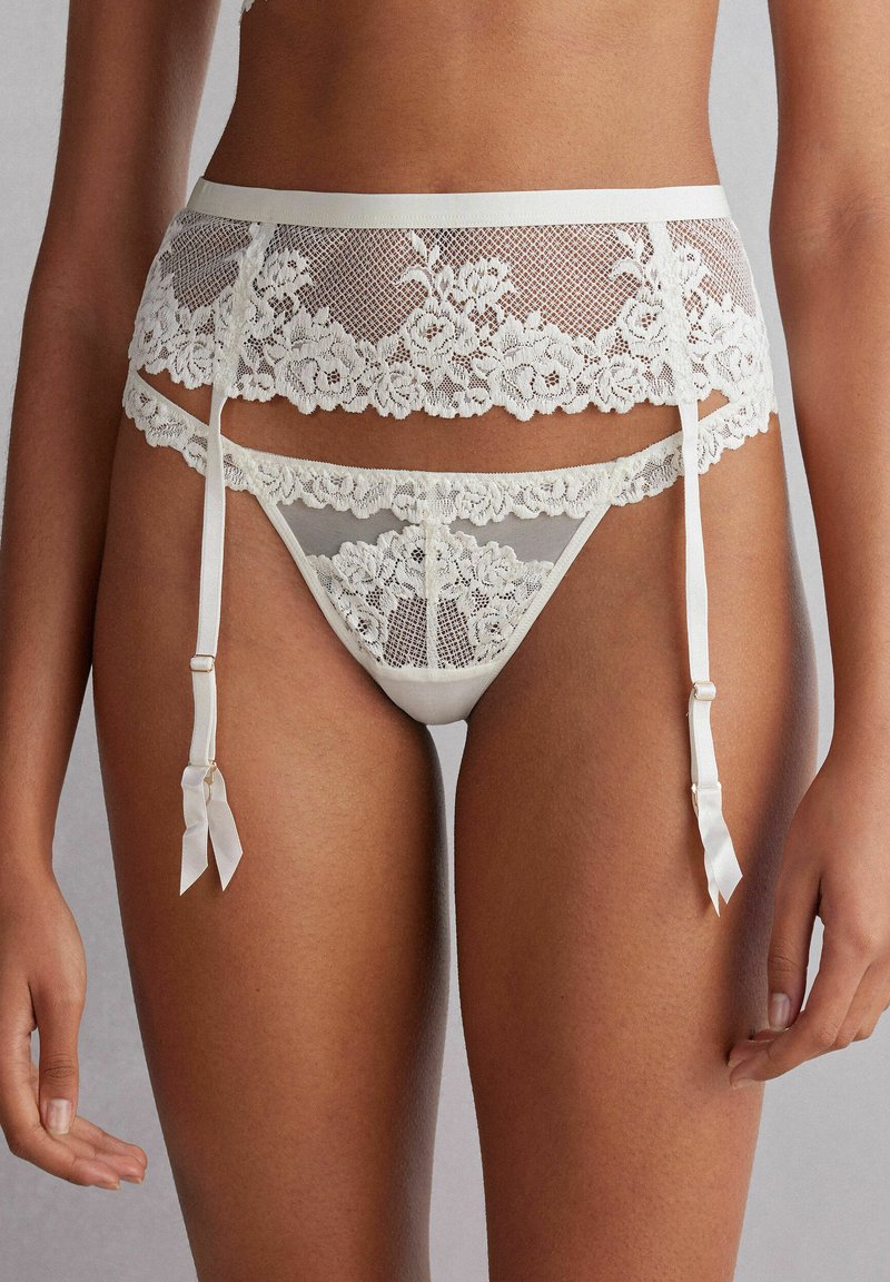 Spetsstrumpeband och stringtrosor i krämfärg, med blommönster, satin-accenter och justerbara remmar. Mjuk, genomskinlig textur genomgående.