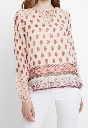 Blusa leggera e trasparente con maniche lunghe. Presenta uno sfondo beige, una stampa paisley marrone e un orlo decorato. Si lega al collo.