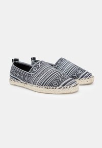 Espadrile u crno-bijelim uzorcima, tekstilna gornja strana s tkanom jutenom potplatom, model na koji se lako obuva, s glatkom teksturom i minimalnim metalnim detaljima.