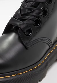 Botte en cuir noir avec lacets rubans noirs brillants, œillets noirs, coutures jaunes le long de la semelle épaisse striée, gros plan sur l’orteil et le côté.