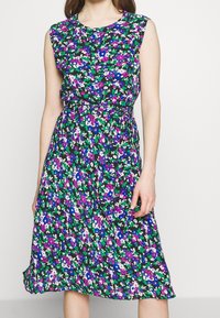 Kwiatowa sukienka w kolorze czarnym, z fioletowymi, niebieskimi i zielonymi kwiatami. Bez rękawów, z talią w fasonie marszczonym i paskiem do związania, lekko opadający dół. Jedwabista tekstura.