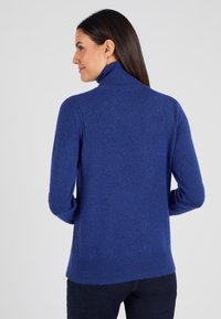 Navyblauwe coltrui van zachte gebreide stof, met geribbelde manchetten en zoom, en een gestructureerd ontwerp voor een aansluitende look.
