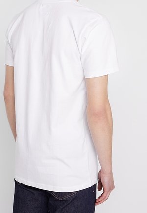 Osoba ubrana w gładką, białą koszulkę z krótkim rękawem i ciemnoniebieskie dżinsy, pokazana od tyłu na jednolitym tle.