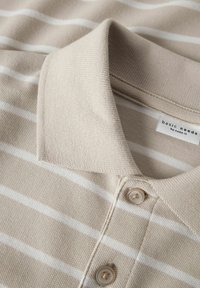 Beige randig polo skjorta med en texturerad tyg, med krage och två knappar. Etikett synlig på insidan av kragen.