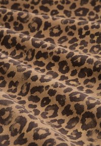 Tela de estampado de leopardo con un fondo marrón claro y manchas irregulares en marrón oscuro, superficie texturizada con un patrón de tejido visible.