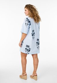 Vestido a rayas azules y blancas con mangas cortas, que presenta estampados florales oscuros. Lleva sandalias de cuña de color claro. Textura de tela suave.