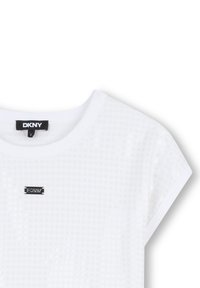 Camiseta blanca de DKNY con un patrón de puntos texturizados, cuello redondo y mangas cortas; cuenta con una pequeña etiqueta de logo negra en la parte frontal.