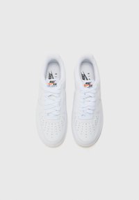 Valkoiset Nike Air Force 1 -tennarit, joissa on sileä nahkapäällinen, rei'itetty varvas, valkoiset nauhat ja kumiotin, jossa on vaalean beigepohja.