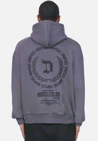 Hall hall featuring a large black graphic print seljal, millel on tekst "HUSTLE CLUB" ja lauri aktsendid; valmistatud pehmest kangast.