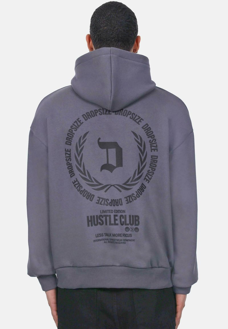 Hall hall featuring a large black graphic print seljal, millel on tekst "HUSTLE CLUB" ja lauri aktsendid; valmistatud pehmest kangast.