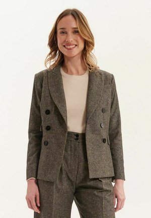 Blazer gris en laine à double boutonnage avec revers crantés, deux poches avant, boutons noirs et coupe ajustée, porté sur un haut beige clair.