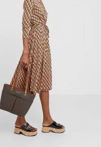 Robe rose avec un motif de feuilles noires et jaunes, taille cintrée et manches 3/4. Sandales noires en patin à plateforme avec une semelle en liège et des boucles décoratives.