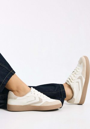 Adidași sintetici bej și alb-crem cu un design texturat, cu talpă de cauciuc și șireturi rotunde. Accentuați cu suprapuneri în nuanțe deschise de bej.