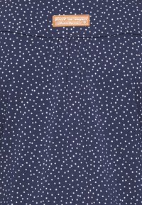 Mörkblåt tygöverdel med vita prickar, en plisserad design och en tan läderetikett med texten "först i vegansk streetwear."