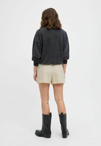Schwarzes Oversize-Sweatshirt mit gerippten Bündchen, kombiniert mit cremfarbenen Shorts mit Lochmuster. Das Model trägt kniehohe schwarze Lederstiefel.