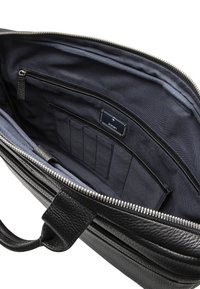 Intérieur d'un sac en cuir noir avec une doublure bleu marine, une poche zippée et plusieurs emplacements pour cartes. Texture lisse et détails de la fermeture éclair en métal.