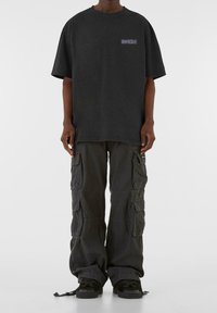 Camiseta de algodón negra de gran tamaño con un pequeño gráfico en el pecho, combinada con pantalones cargo oscuros que cuentan con múltiples bolsillos y puños ajustables.