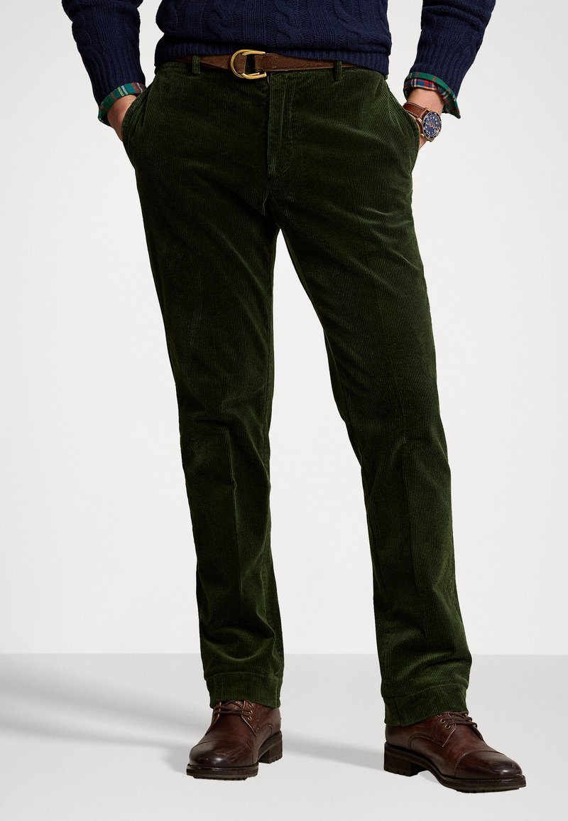 Grønne kordfløjl bukser med en struktureret overflade, lige ben design, forlommer og et brunt bælte, der fremhæver taljen.