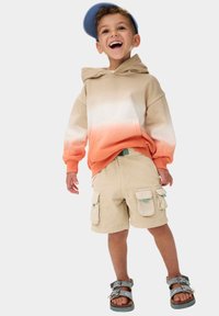 Beige och orange ombre-hoodie med en känguruficka, parat med ljus khaki cargo shorts med två sidofickor, och grå sandaler.