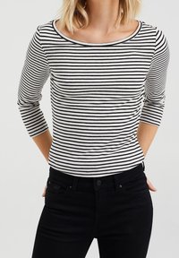 Svart och vit randig långärmad skjorta med breda axlar, gjord av mjuk bomull, i kombination med svarta jeans.