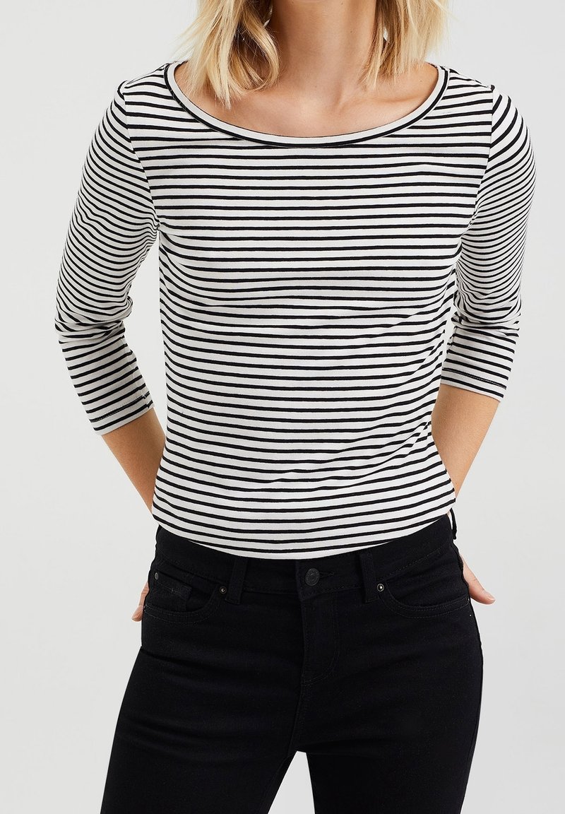 Svart och vit randig långärmad skjorta med breda axlar, gjord av mjuk bomull, i kombination med svarta jeans.