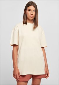 Beige oversized t-shirt med korta ärmar, rund halsringning och en mjuk bomullstextur. Enkelt design, utan mönster eller accenter.