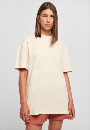 Beige oversized t-skjorte med korte ermer, rund hals, og en glatt bomullstekstur. Enkel design, uten mønstre eller detaljer.