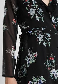 Schwarzes Kleid mit floralem Druck in Blau, Rot und Grün. Lange, durchsichtige Ärmel, Wickeldesign, inklusive eines passenden Bindegurtes, weiche Textur.