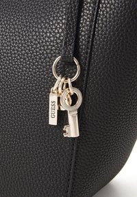 Zwarte neplederen handtas met een textuur, ronde vorm en goudkleurige accenten zoals sleutels en labels.