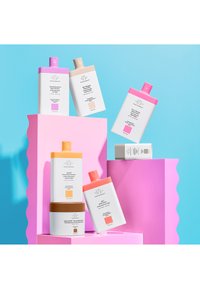 Sieben bunte Hautpflegeprodukte sind auf pinken geometrischen Ständern vor einem hellblauen Hintergrund ausgestellt, wobei ihre Verpackungsdesigns hervorgehoben werden.