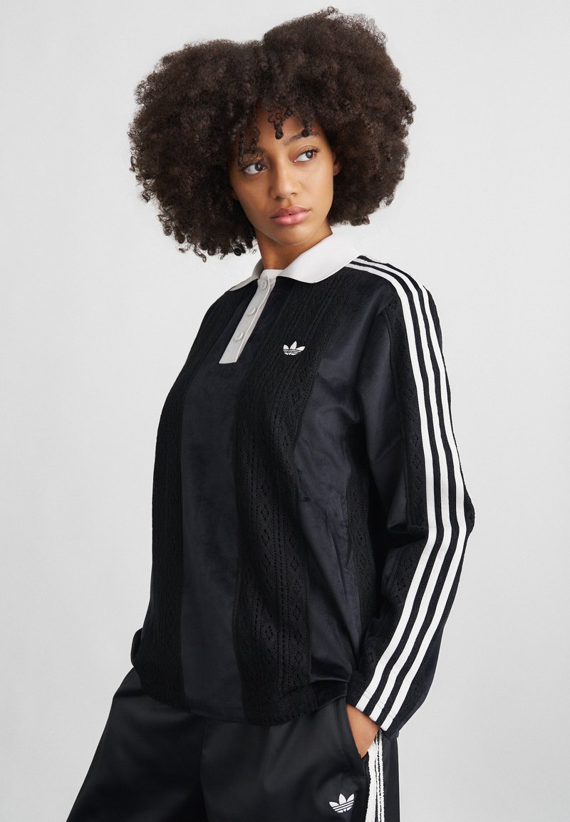 Pulover sport negru cu guler alb, textură cu model dantelat pe față și trei dungi albe pe fiecare mânecă.