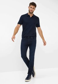 Polo shirt navy con maniche corte, abbinato a jeans blu scuro e sneakers navy. Design semplice con colletto classico e vestibilità rilassata.