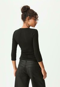 Schwarzes Langarmoberteil mit rundem Ausschnitt, figurbetontem Design und weichem Stoff, kombiniert mit hochgeschnittenen schwarzen Jeans mit Gesäßtaschen.