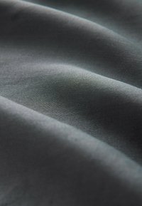 Dunkelgrauer Stoff mit einer glatten Textur, der sanfte Falten und einen subtilen Glanz aufweist, der das Licht auf sanfte, gedämpfte Weise einfängt.