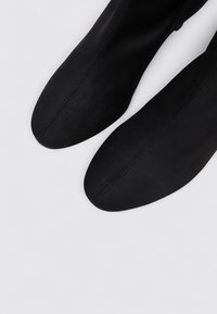 Black knee-high boots made of soft suede with a smooth finish, featuring a pointed toe and minimal stitching detail.