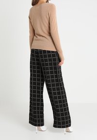 Beżowy sweter z długimi rękawami i prążkowanym wykończeniem, w połączeniu z czarnymi spodniami o szerokich nogawkach z białym wzorem w kratę oraz białymi szpilkami.