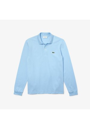 Ljusblå långärmad pikétröja med krage, med en grön Lacoste-logotyp på vänster bröstområde. Tillverkad av mjukt bomullsmaterial.