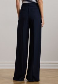 Granatowe spodnie o szerokich nogawkach z gładką fakturą, wyposażone w dwie tylne kieszenie, wysoki stan i subtelne zakładki dla lepszej struktury.