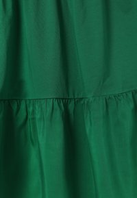 Tissu vert avec un détail de couture froncée créant de subtils volants et une variation de texture sur un matériau lisse.