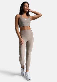 Beige Sport-BH und hochgeschnittene Leggings aus einem glatten Material mit gerippten Akzenten, kombiniert mit weißen Sportschuhen.