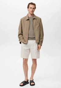 Giacca di cotone beige, maglione grigio a coste, pantaloni corti bianchi e sandali neri. Vestibilità moderna, design minimalista, texture liscia e senza motivi visibili.