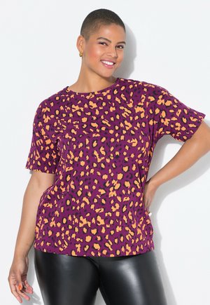 Camiseta de tirantes corta morada con estampado de leopardo negro y naranja, con un ajuste relajado y textura suave, combinada con leggins negros.